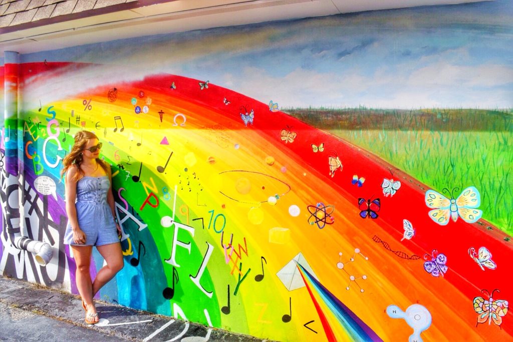 woman standing in front of rainbow mural